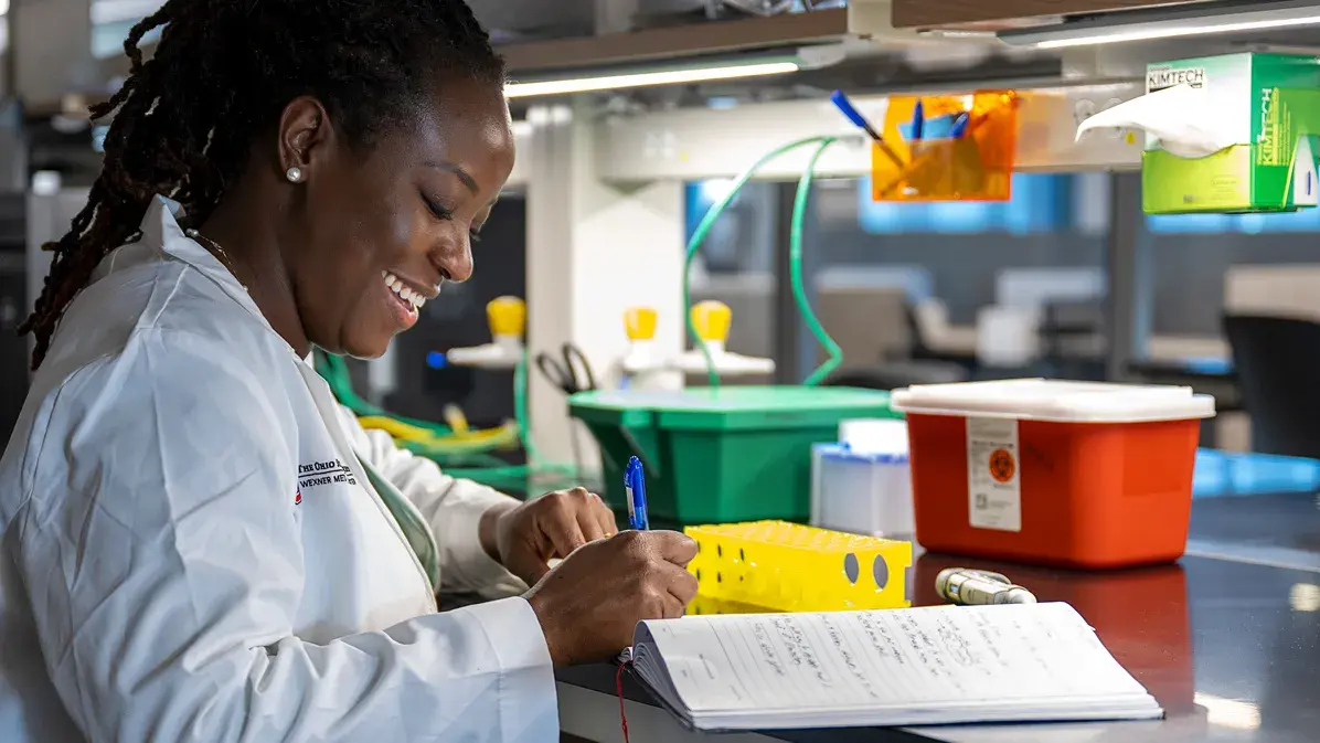 woman in a lab coat documenting notes in a notebook in a laboratory setting