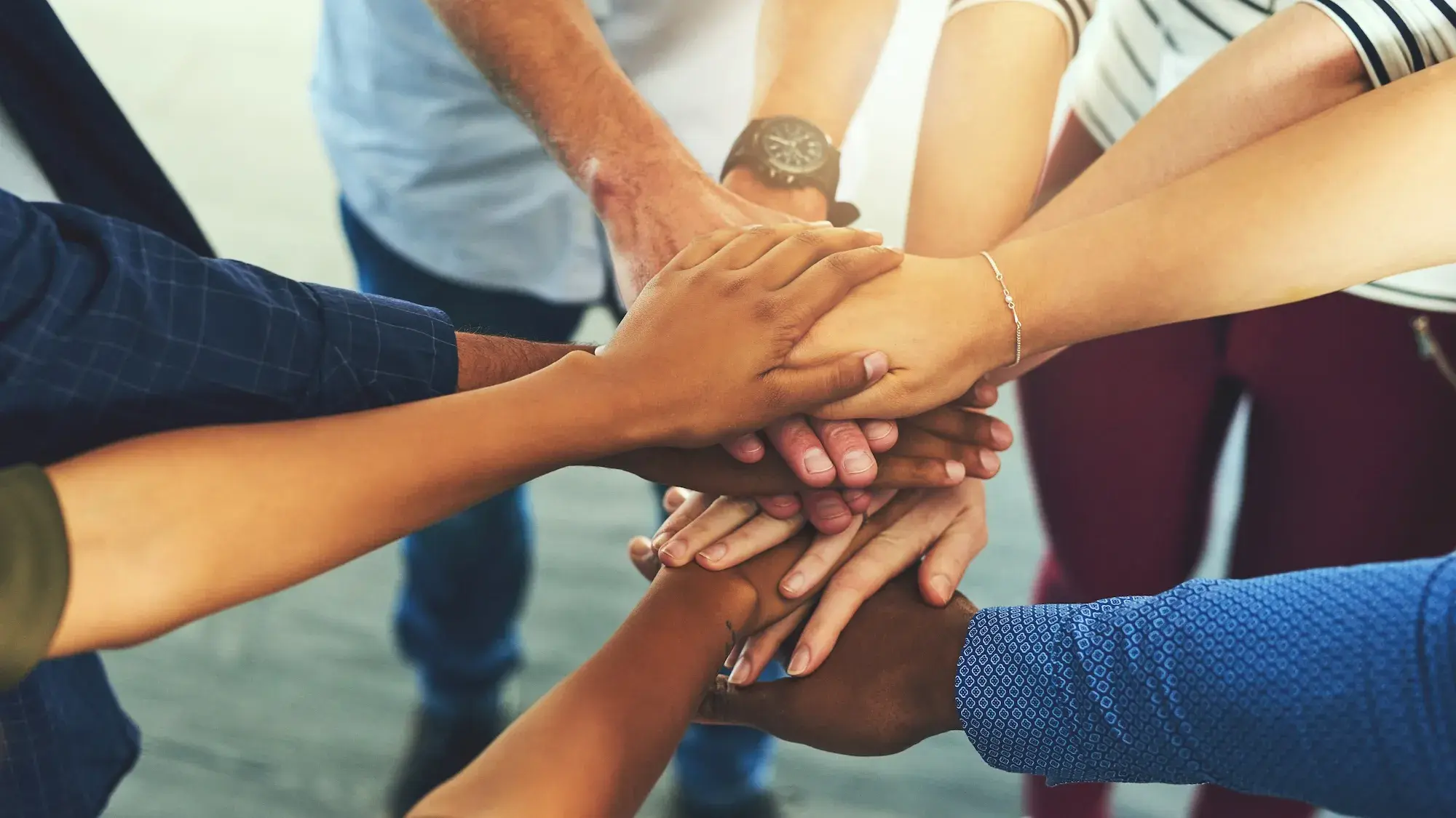 Several people standing in a circle, each putting a hand or two on top of eachother in the middle