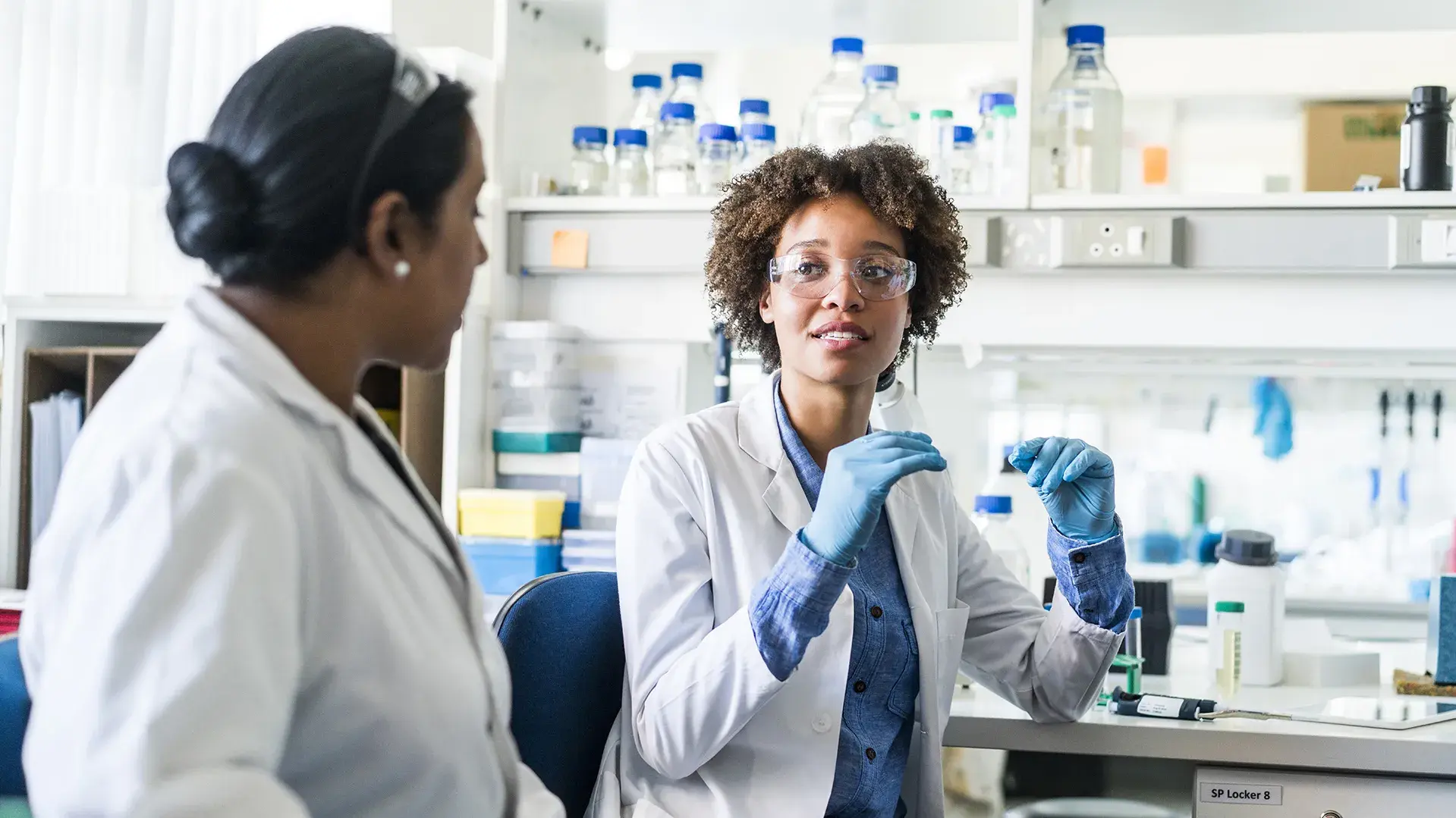 Two researchers wearing safety gear in a lab talking